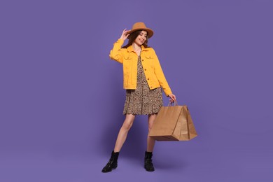 Stylish young woman with shopping bags on purple background