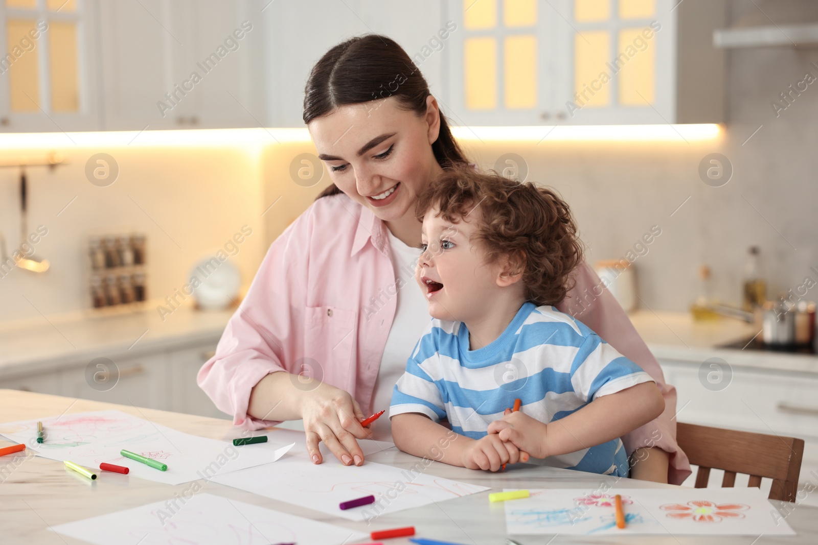 Photo of Mother and her little son drawing with colorful markers at table in kitchen