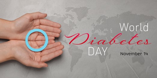 Image of World Diabetes Day. Woman holding blue paper circle at grey table with world map, top view. Banner design