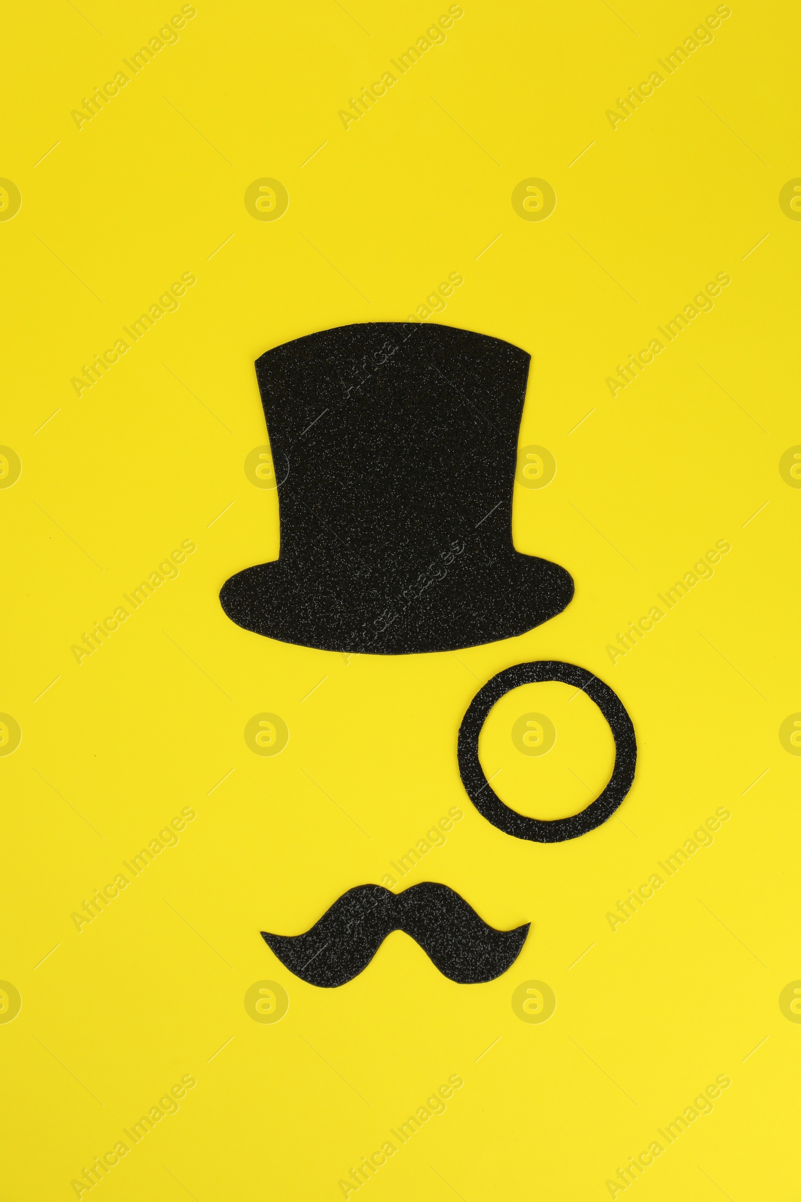 Photo of Man's face made of fake mustache, hat and monocle on yellow background, top view