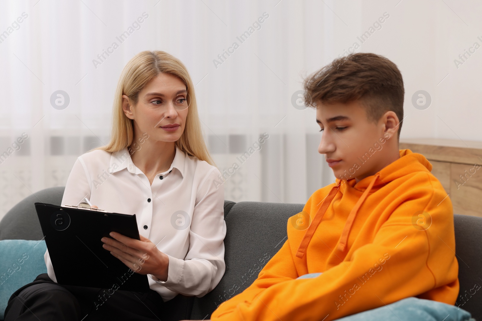 Photo of Psychologist working with teenage boy on sofa in office