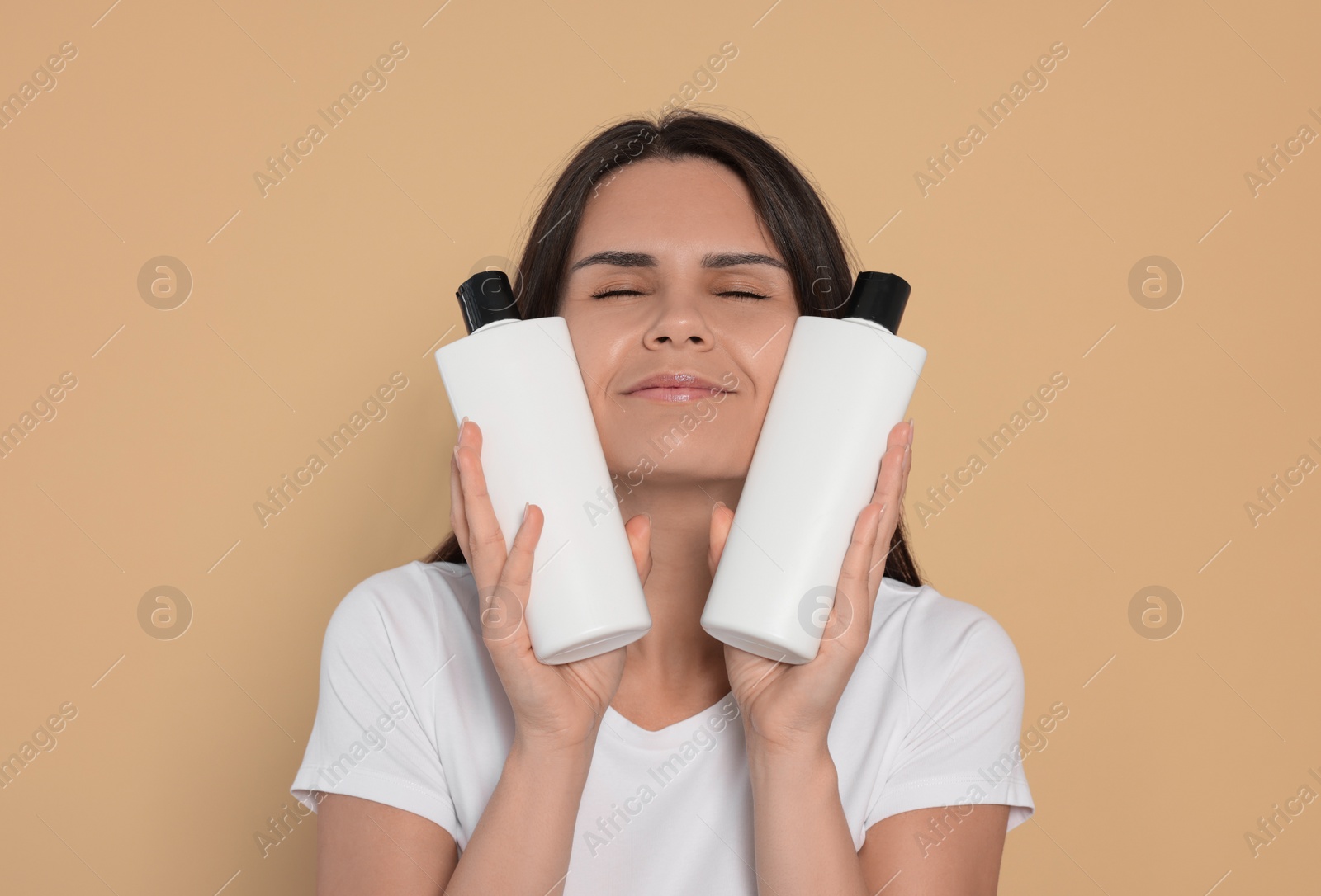 Photo of Beautiful young woman holding bottles of shampoo on beige background