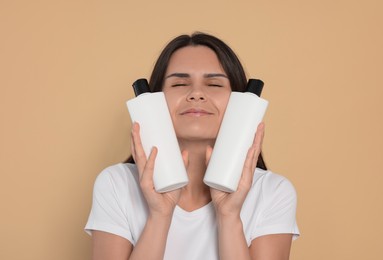 Photo of Beautiful young woman holding bottles of shampoo on beige background