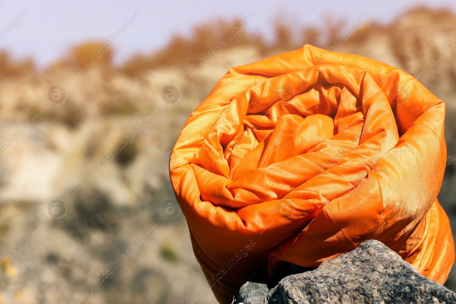 Photo of Orange sleeping bag on rock outdoors, space for text. Camping equipment