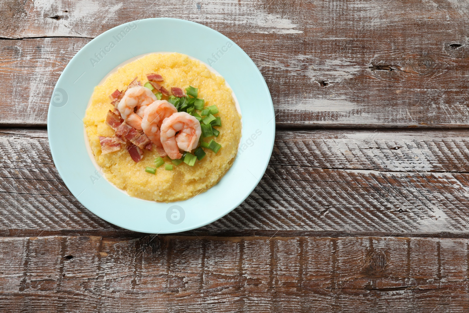 Photo of Plate with fresh tasty shrimps, bacon, grits and green onion on wooden table, top view. Space for text