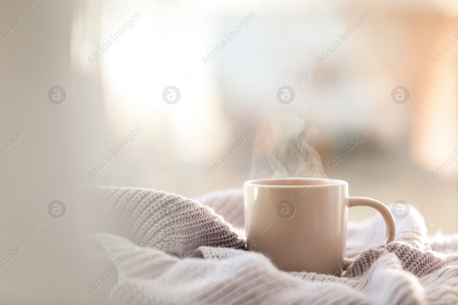 Photo of Cup of coffee and knitted sweater near window in morning. Space for text