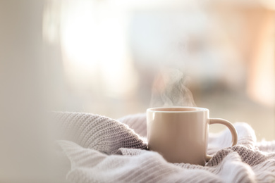 Photo of Cup of coffee and knitted sweater near window in morning. Space for text