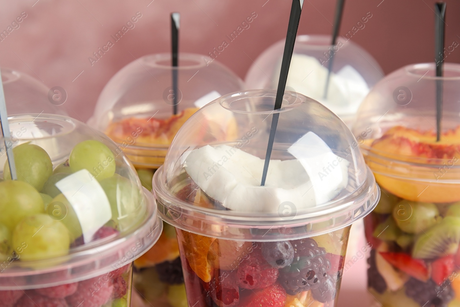 Photo of Fresh tasty fruit salad in plastic cups on pink background, closeup