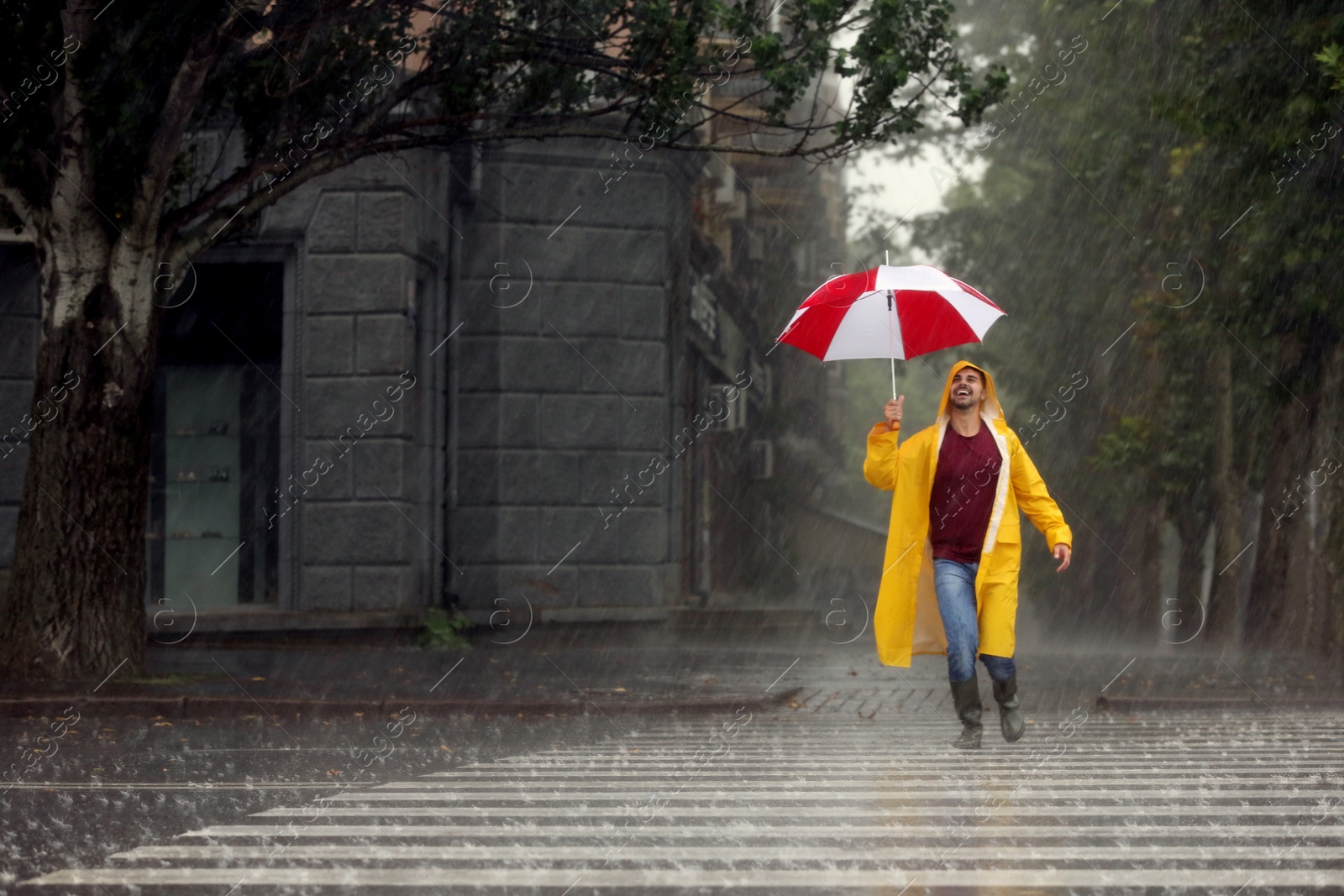 Photo of Happy young man with colorful umbrella outdoors on rainy day