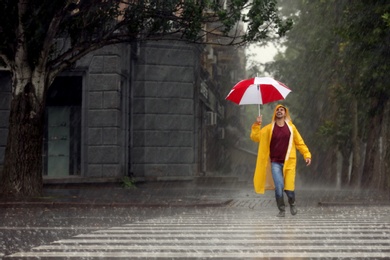 Happy young man with colorful umbrella outdoors on rainy day