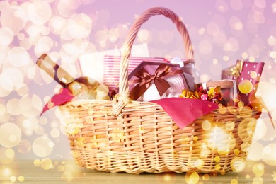 Image of Wicker basket with gifts, wine and food against blurred festive lights. Christmas celebration