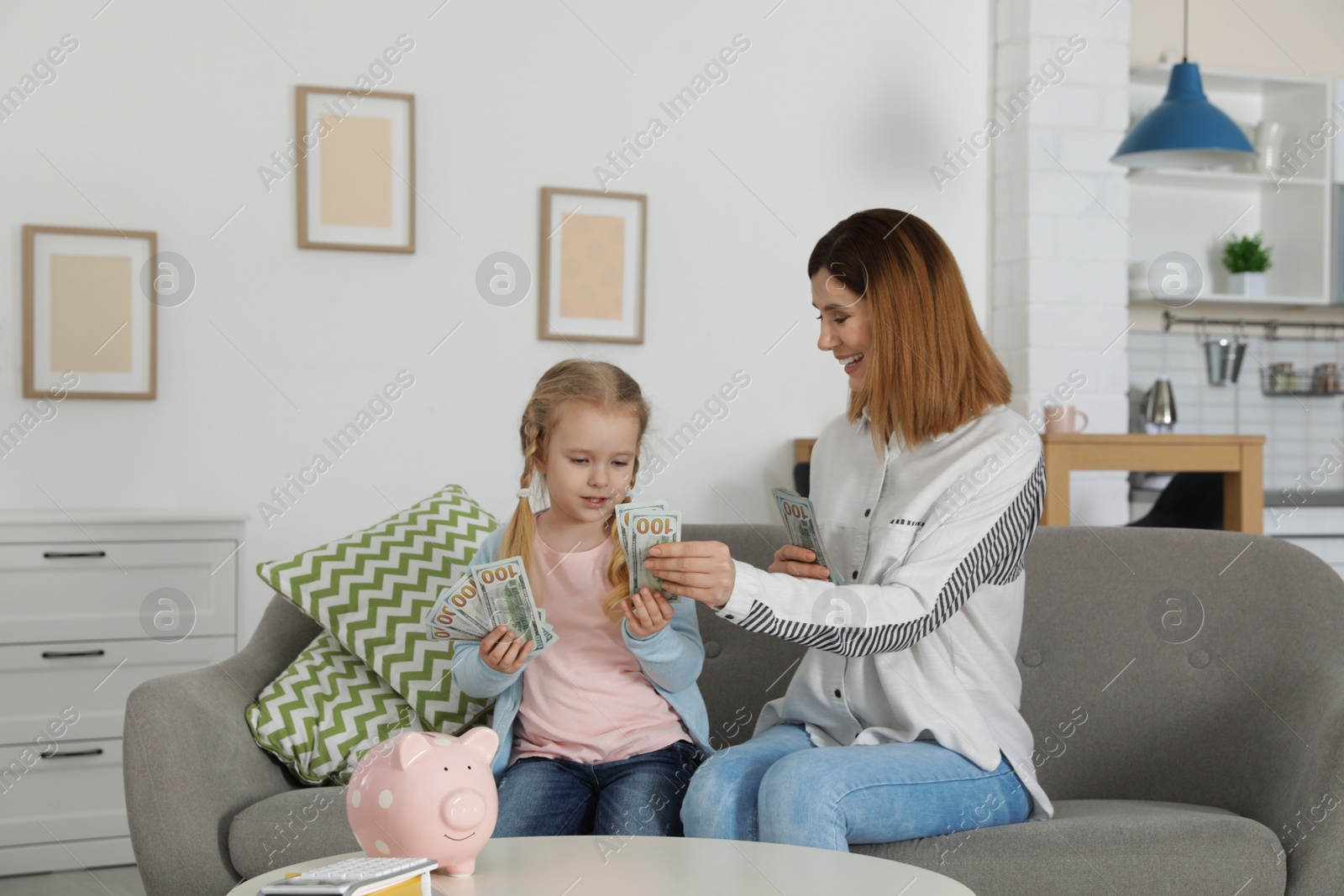 Photo of Mother and daughter counting money on sofa indoors