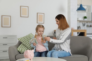 Photo of Mother and daughter counting money on sofa indoors