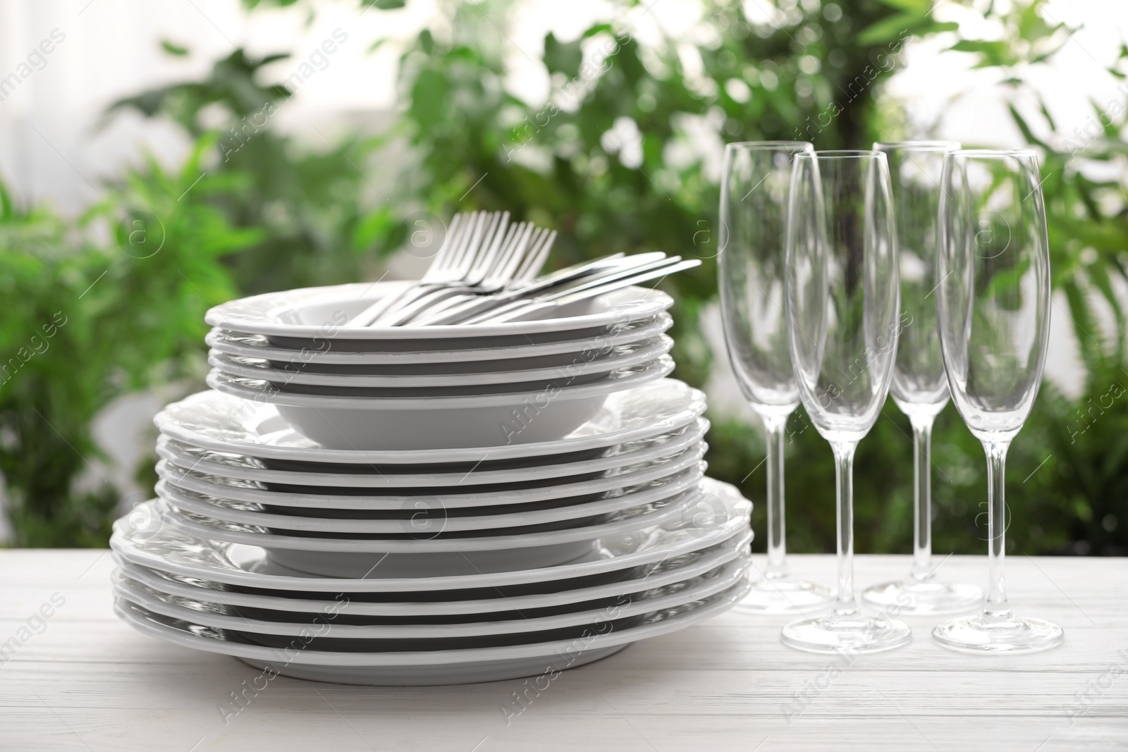 Photo of Set of clean dishware, cutlery and champagne glasses on white table against blurred background
