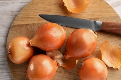 Photo of Tray with ripe onions and knife on wooden table, top view