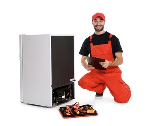 Photo of Male technician with clipboard and tools near broken refrigerator on white background