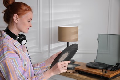 Young woman with vinyl disc near turntable at home