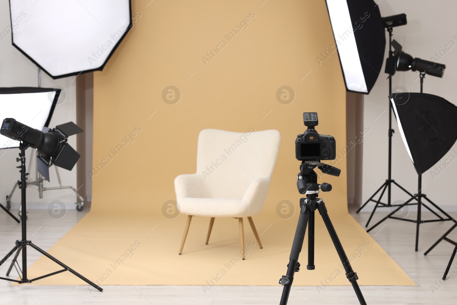 Photo of Camera on tripod, armchair and professional lighting equipment in modern photo studio, space for text