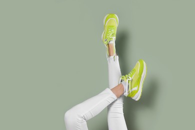 Woman wearing new stylish sneakers on light green background, closeup. Space for text