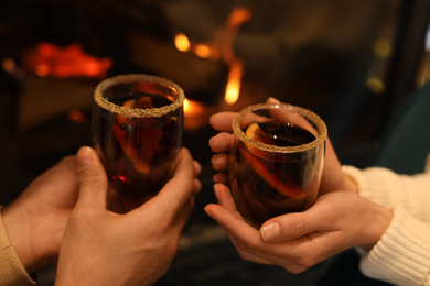 Couple with tasty mulled wine near fireplace indoors, closeup