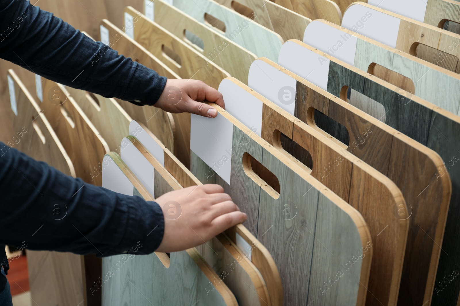 Photo of Man choosing wooden flooring among different samples in shop, closeup