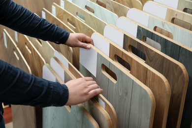 Photo of Man choosing wooden flooring among different samples in shop, closeup