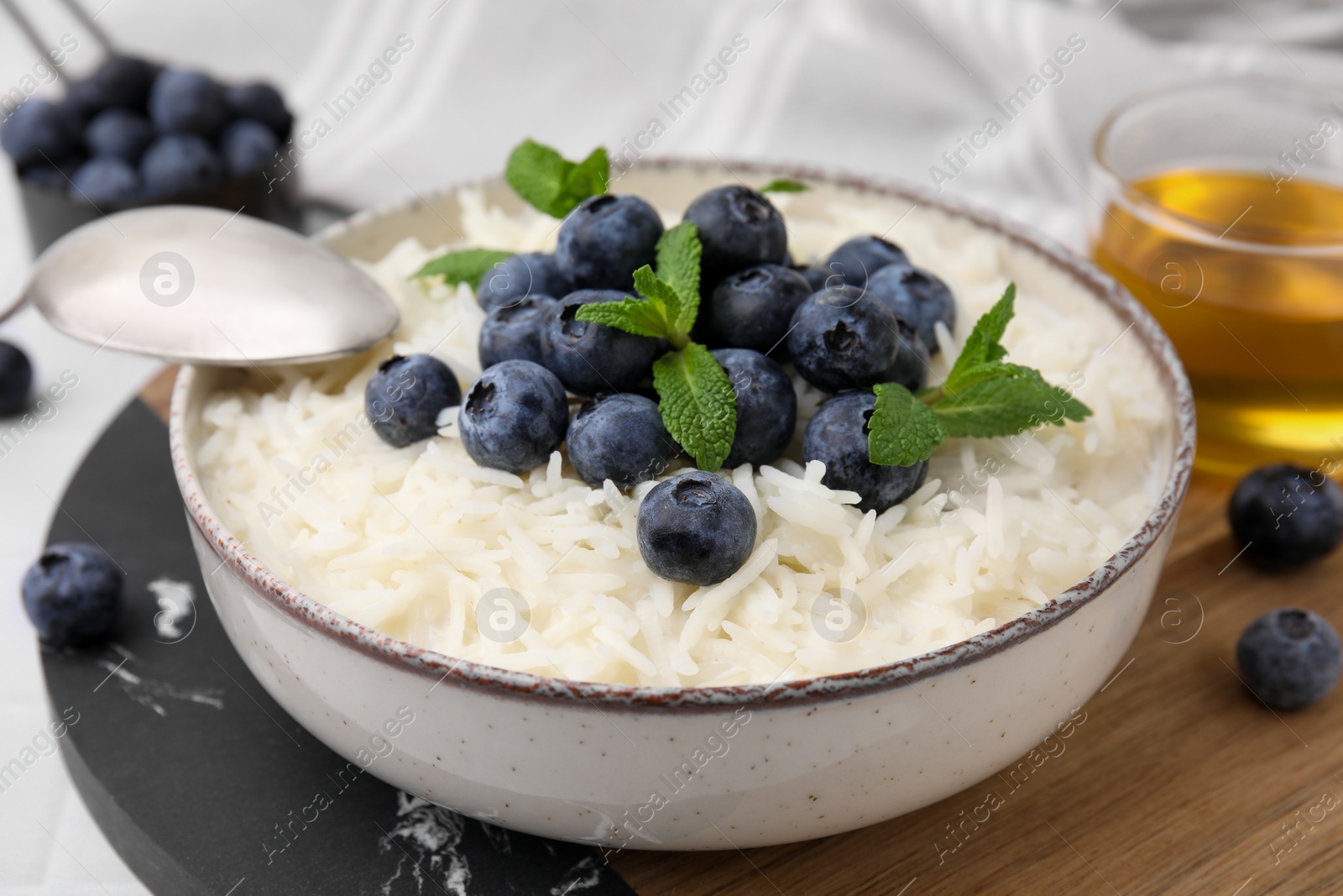 Photo of Bowl of delicious rice porridge with blueberries and mint served on table, closeup