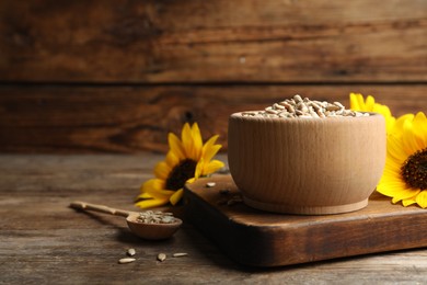 Photo of Raw peeled sunflower seeds and flowers on wooden table. Space for text