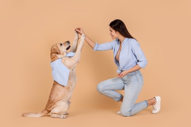 Happy woman playing with cute Labrador Retriever against beige background