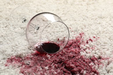 Photo of Overturned glass and spilled red wine on white carpet, closeup