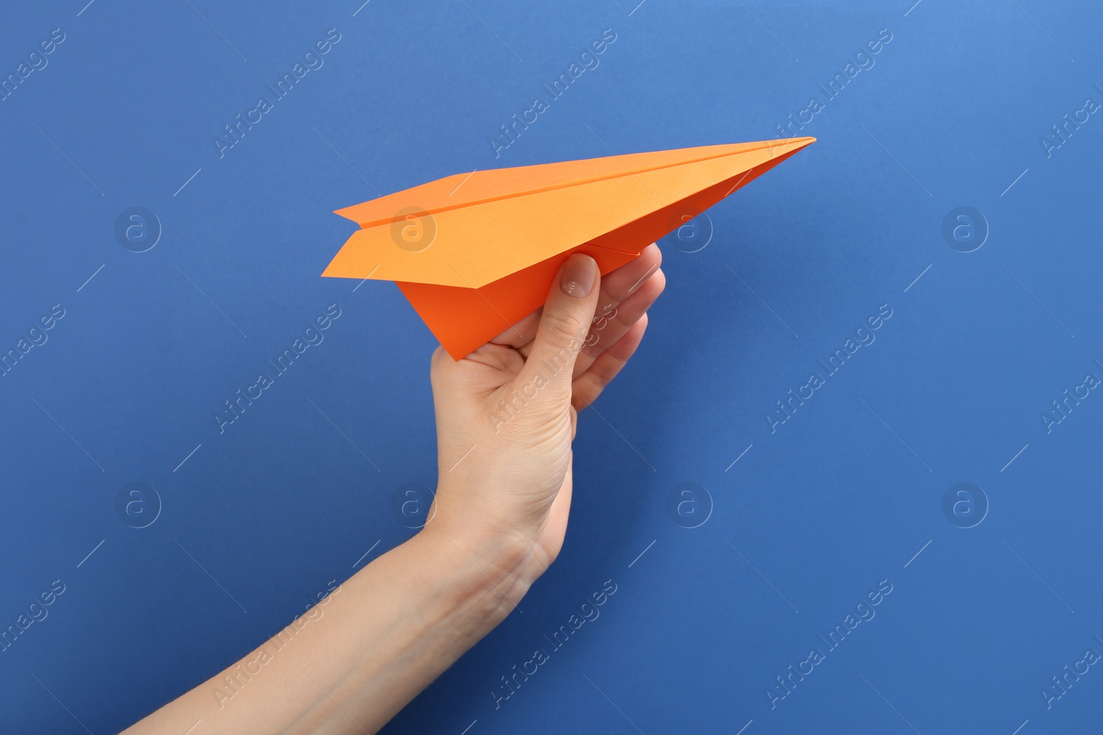 Photo of Woman holding paper plane on blue background, closeup