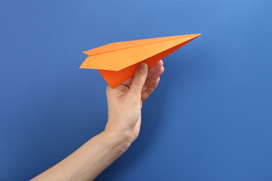 Woman holding paper plane on blue background, closeup