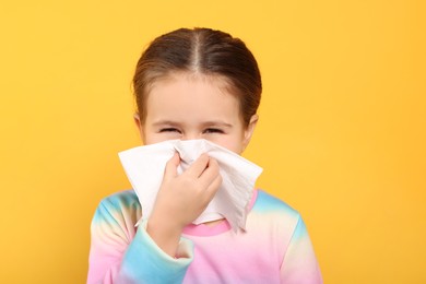 Girl blowing nose in tissue on orange background. Cold symptoms