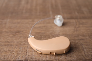 Photo of Hearing aid on wooden table, closeup. Medical device