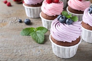 Photo of Sweet cupcakes with fresh berries on wooden table. Space for text