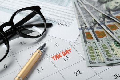 Photo of Calendar with date reminder about tax day, documents, money, pen and glasses, closeup