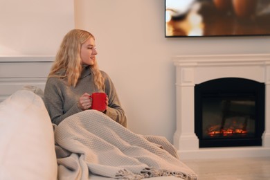 Photo of Young woman with cuphot drink resting near fireplace at home