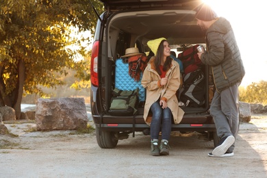 Young couple packing camping equipment into car trunk outdoors