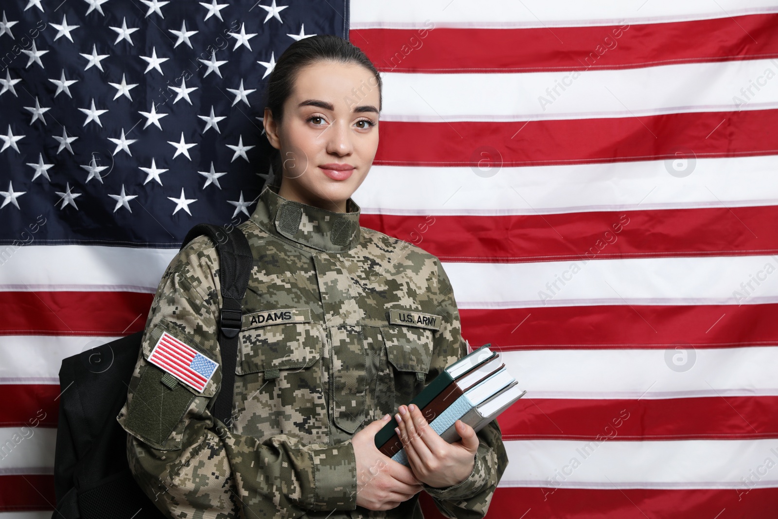 Photo of Female soldier with backpack and books near flag of United States, space for text. Military education