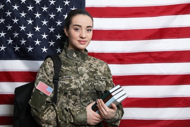 Female soldier with backpack and books near flag of United States, space for text. Military education