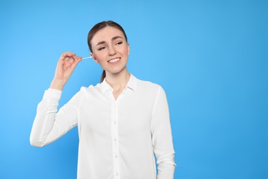Photo of Young woman cleaning ear with cotton swab on light blue background. Space for text