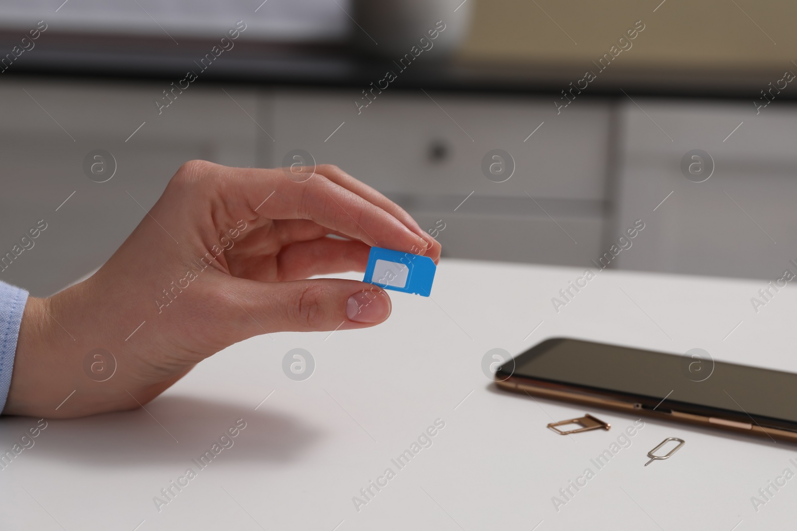 Photo of Woman with SIM card at white table indoors, closeup