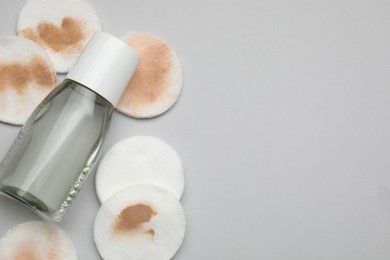 Photo of Bottle of makeup remover, clean and dirty cotton pads on light grey background, flat lay. Space for text