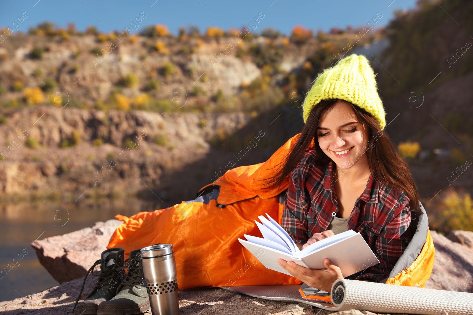 Photo of Female camper in sleeping bag reading book outdoors. Space for text