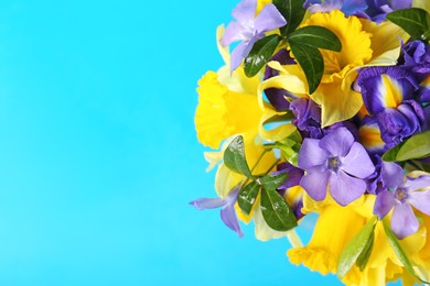 Bouquet of beautiful yellow daffodils, iris and periwinkle flowers on light blue background, top view. Space for text
