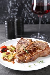 Delicious fried beef meat, vegetables and glass of wine on grey table