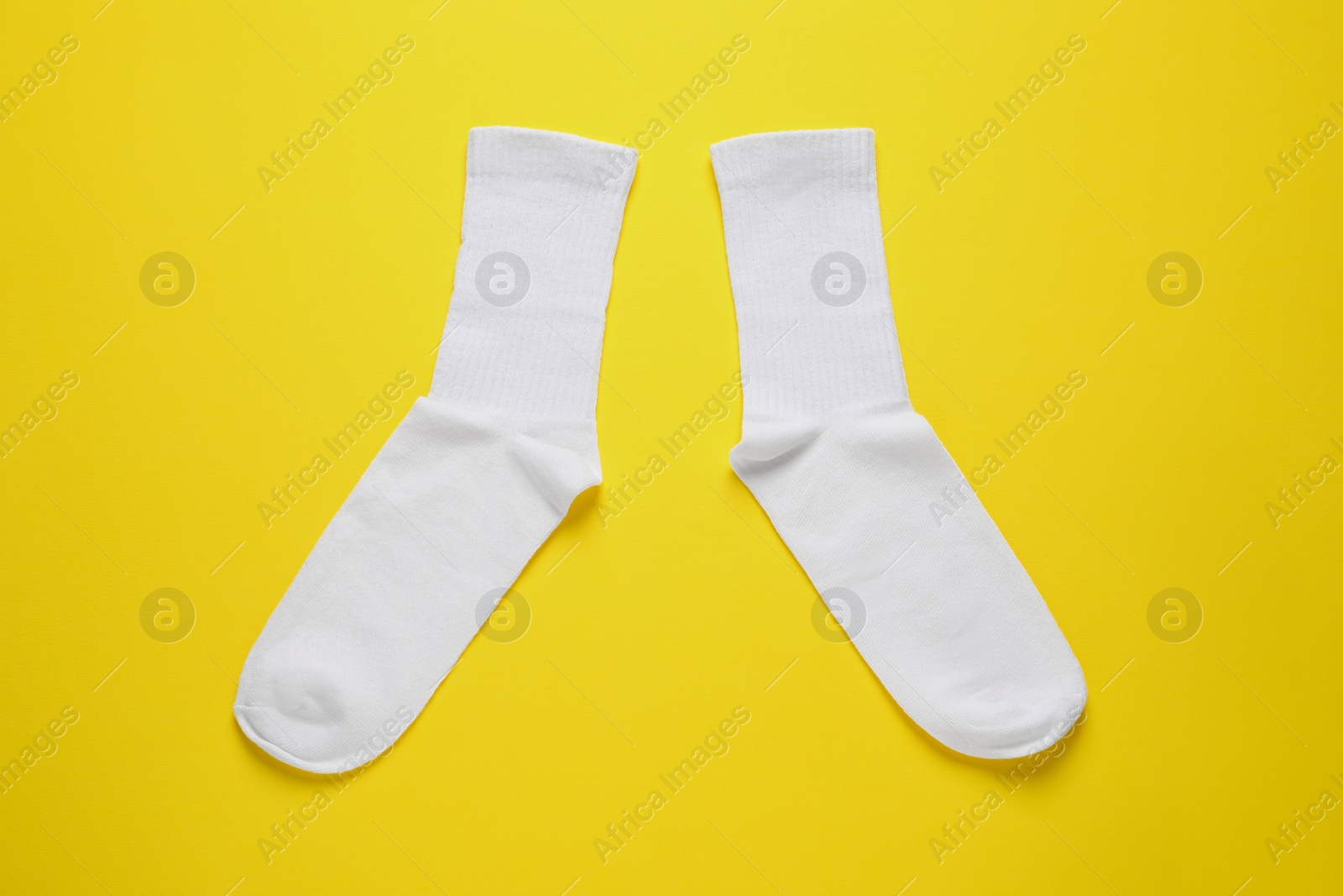 Photo of Pair of white socks on yellow background, flat lay