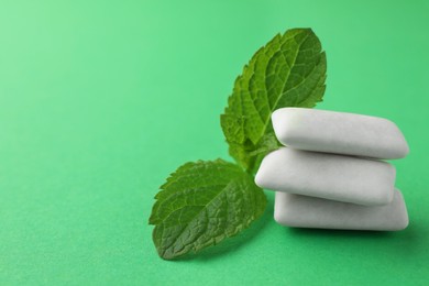 Tasty white chewing gums and mint leaves on green background, closeup. Space for text