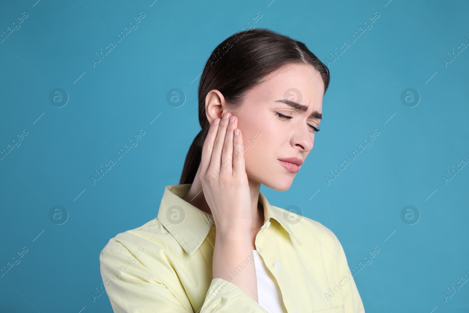 Photo of Young woman suffering from ear pain on light blue background