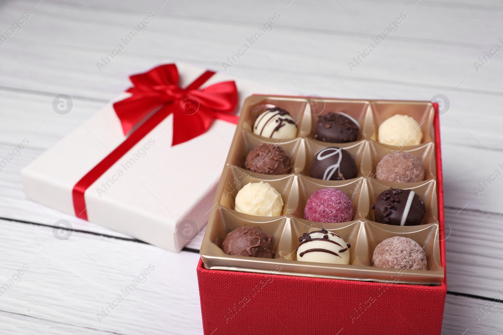Red box with tasty chocolate candies on white wooden table, closeup Photo of Red box with tasty chocolate candies on white wooden table, closeup